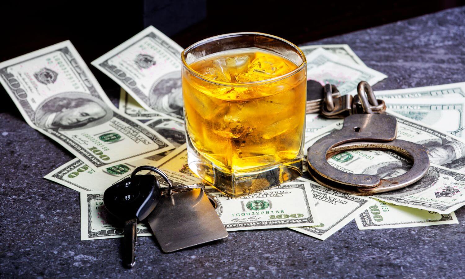 A glass of whiskey with ice on scattered dollar bills and car keys.