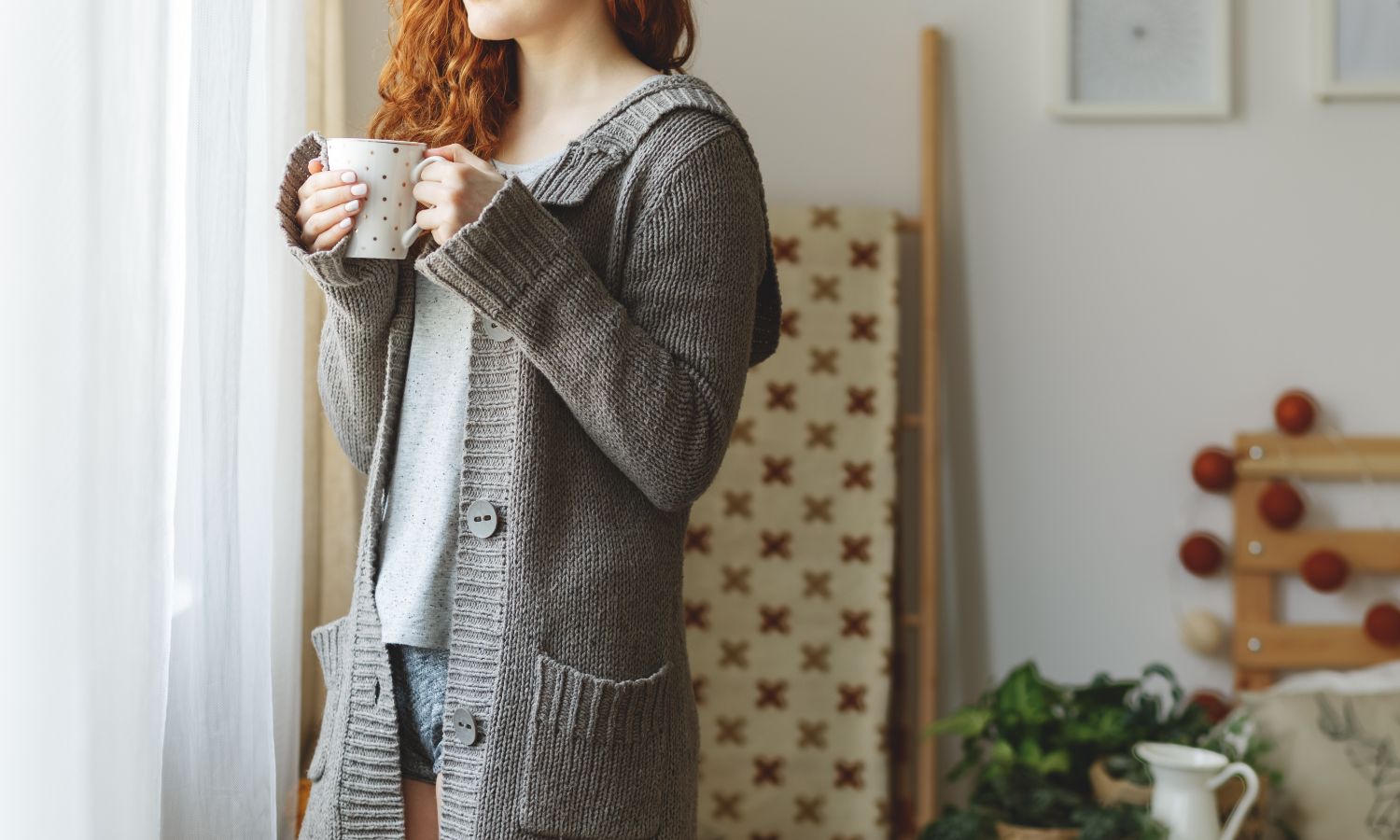 Woman in cozy cardigan holding a warm mug indoors.
