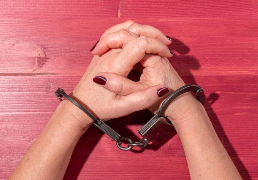 Hands clasped in handcuffs on a wooden surface.